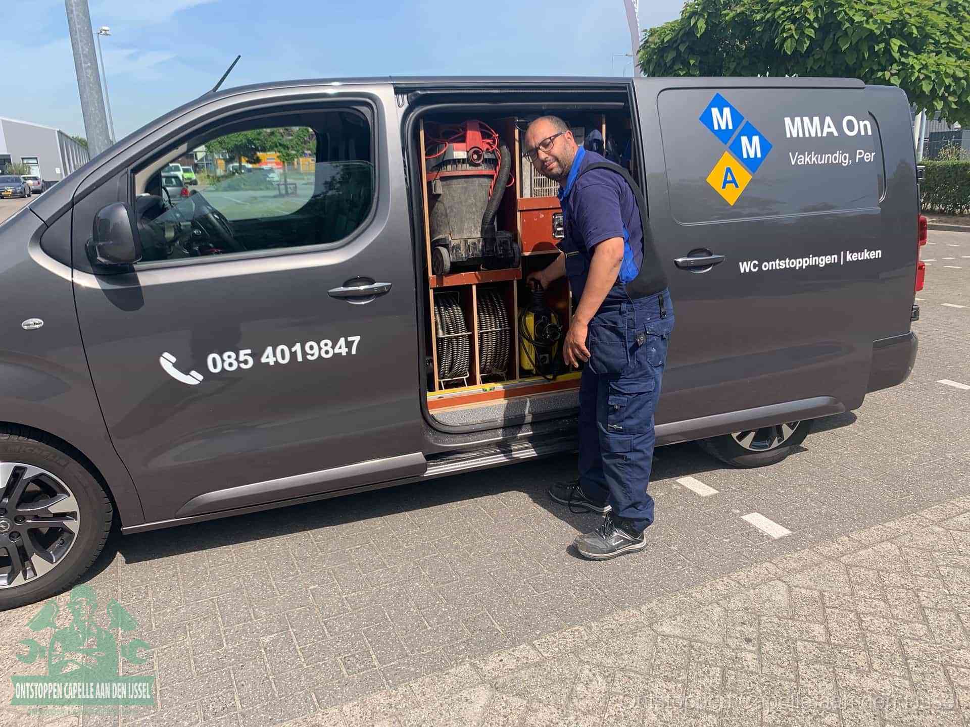 Een monteur bij de open schuifdeur van zijn bedrijfsbus op een parkeerplaats, klaar om de oorzaak van terugkerende afvoerverstoppingen aan te pakken in Capelle aan den IJssel