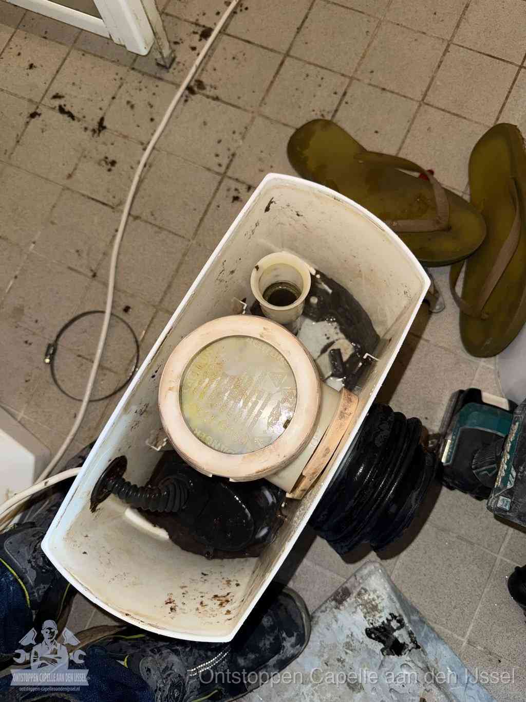 Een gedemonteerde toiletpot op de vloer met ontstoppingsveer en gereedschap ernaast, het verwijderen van een vastzittend voorwerp uit de wc in Capelle aan den IJssel