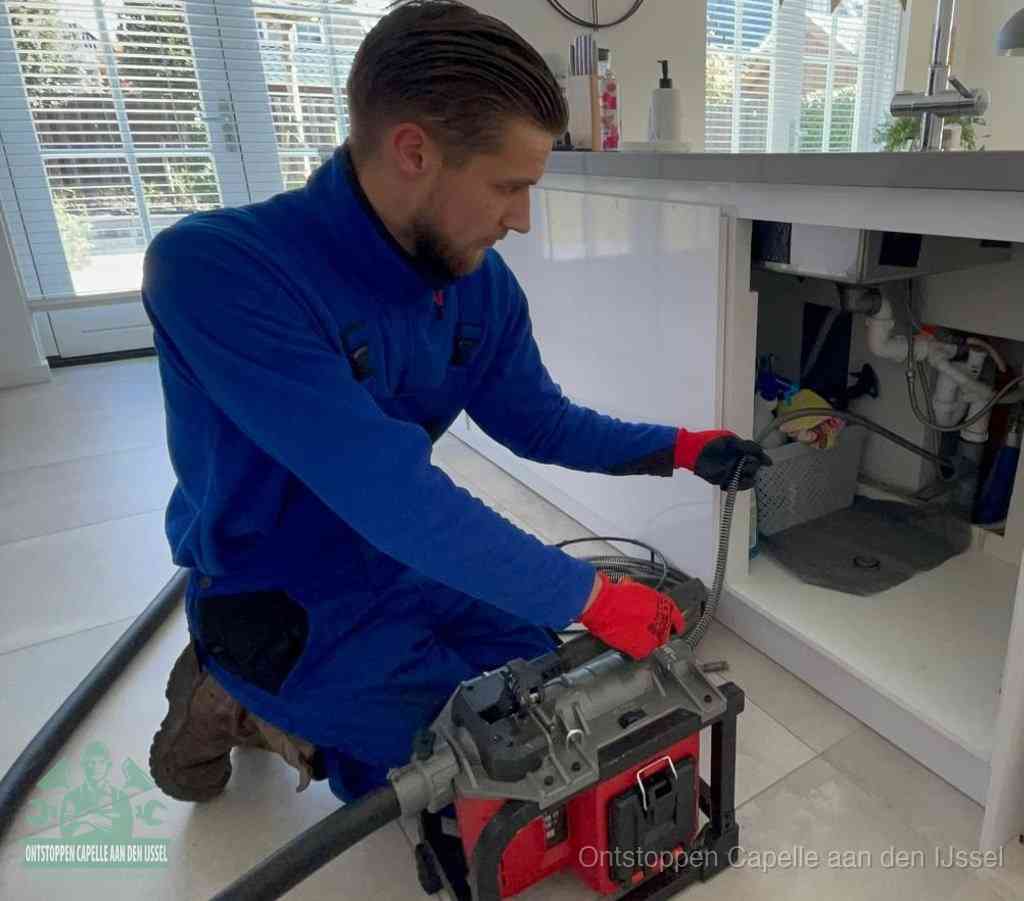 Een monteur met rode handschoenen knielt in een keuken en voert een elektrische ontstoppingsveer in tijdens het professioneel afvoer ontstoppen in Capelle aan den IJssel
