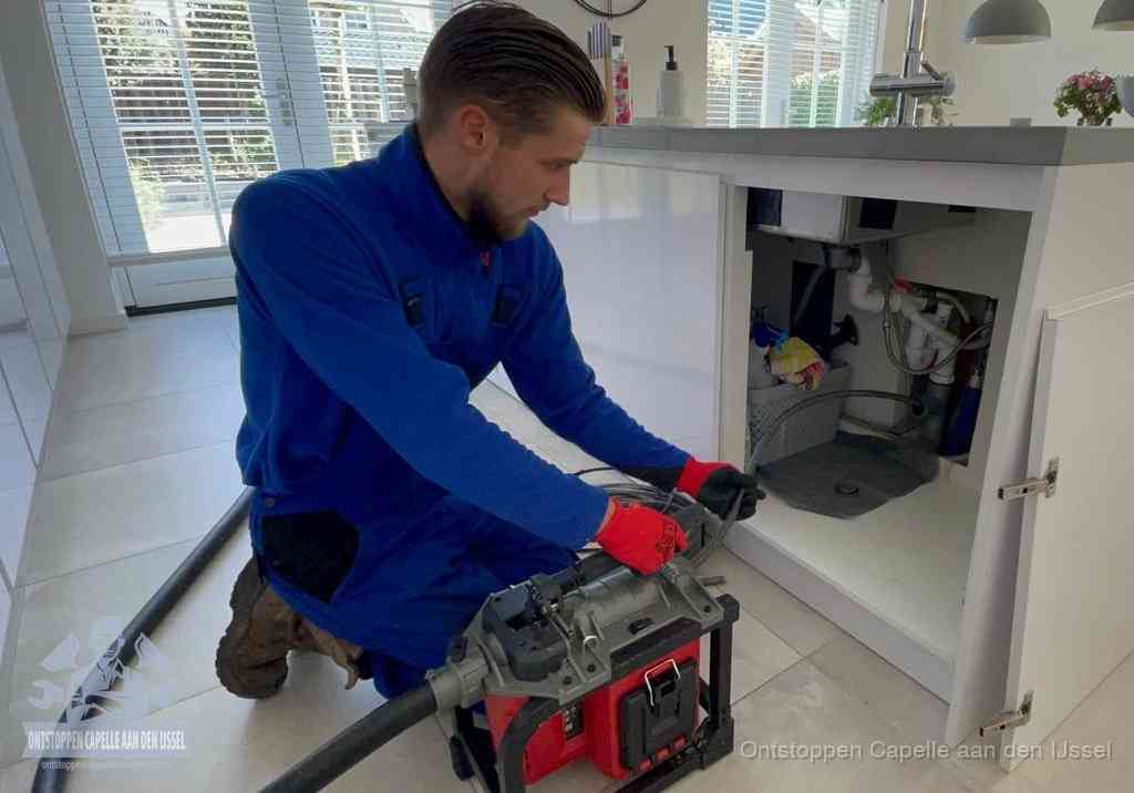 Een monteur voert een professionele elektrische ontstoppingsmachine in de afvoer onder de spoelbak tijdens het gootsteen ontstoppen in Capelle aan den IJssel